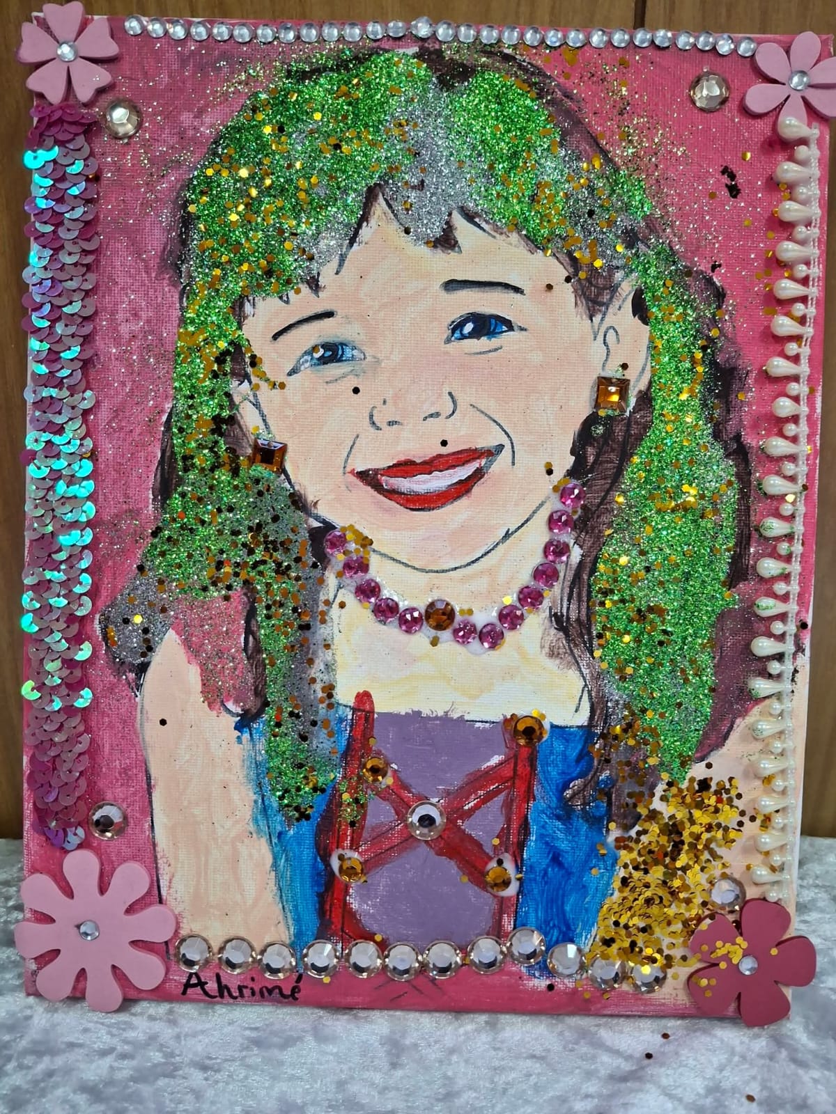 An expressive self-portrait made in a Canvas Hope workshop — a painted face with glitter hair, gems, beads and flowers on a bright canvas