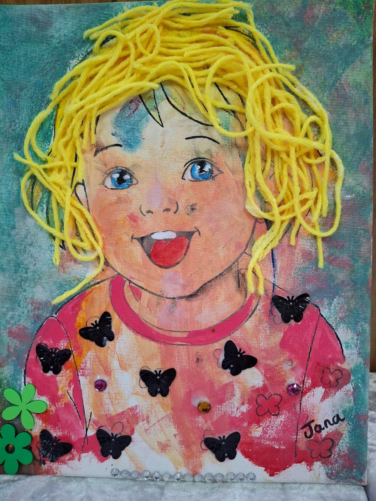 A child's expressive self-portrait with wool hair, butterflies and gems, made at a Canvas Hope workshop